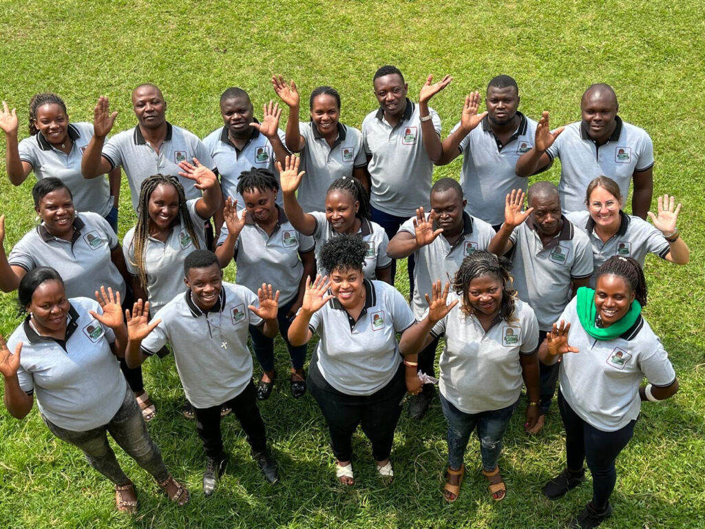 A group of people wearing matching gray polo shirts stands on grass, smiling and waving at the camera. Network Marketing Mastery