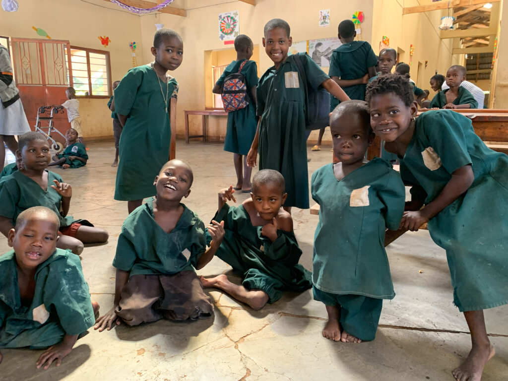 A group of children in green uniforms smile and pose inside a classroom with colorful decorations on the walls. Network Marketing Mastery